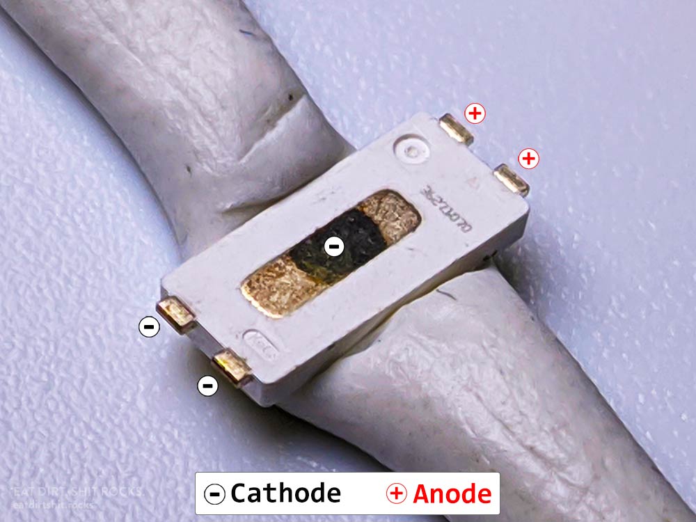 Underside of one of these LEDs. The oblong thermal pad is also part of the cathode (negative terminal). The other LEDs I've removed from the same bit of tape don't have a dark spot in the middle of the thermal pad. I'd guess it's corrosion.