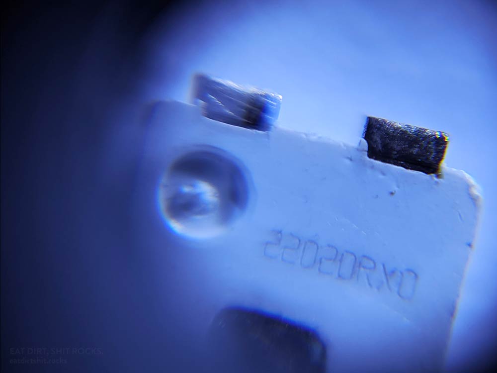 Closeup of the anode (positive) end of the underside of one of these LEDs. The bellybutton-like feature is probably an 'anode mark' and the text seems to be a serial number as it varies from one LED to the next.