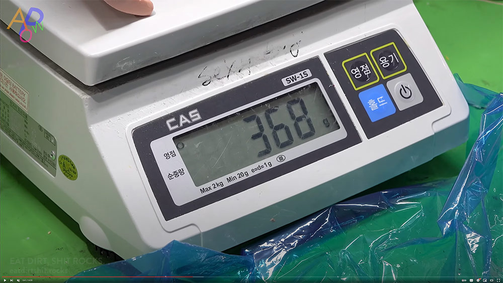 Screen capture of the most recent APoW video showing a worker weighing a portion of flesh-colored silicone that's about to be made into children's meal trays.